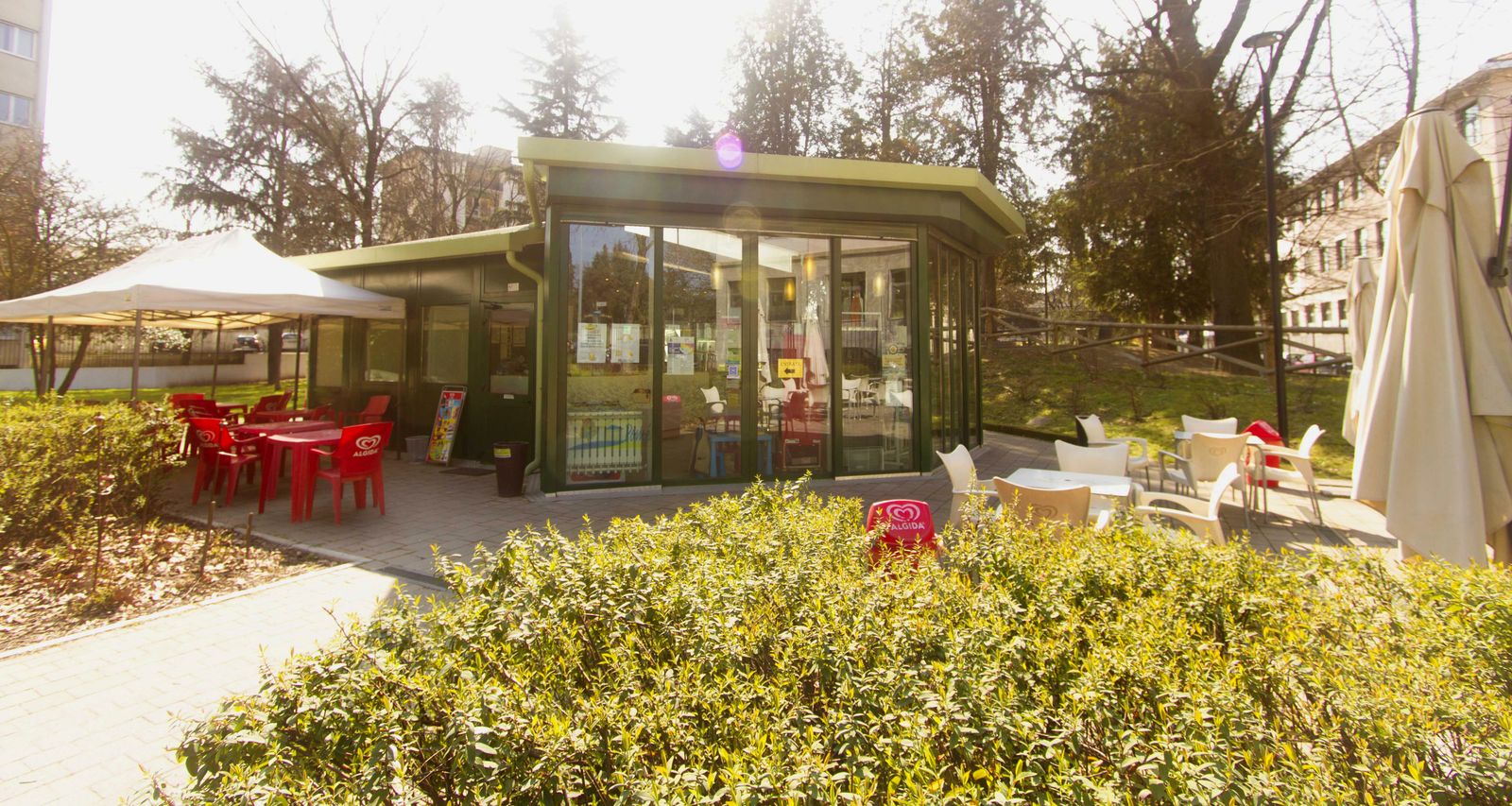 Il chiosco verde con le vetrate nel Parco De Vecchi, con i tavolini fuori e la siepe davanti